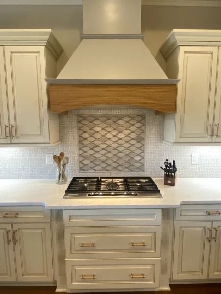 Modern kitchen with cream cabinets, stainless range hood, mosaic backsplash, and gas cooktop