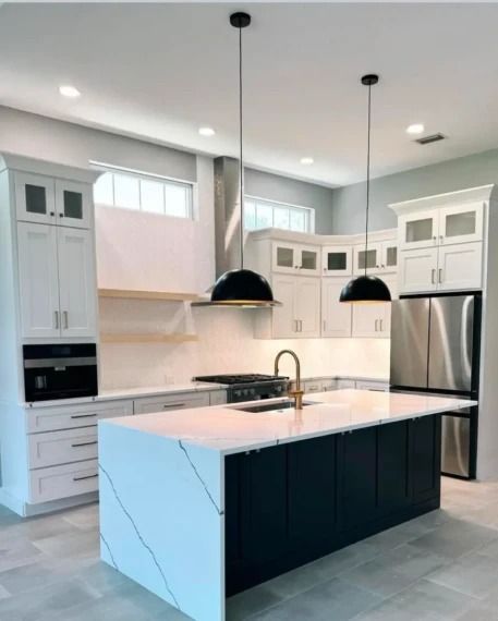 Modern white kitchen with dark island, stainless steel appliances, pendant lights, and marble countertops