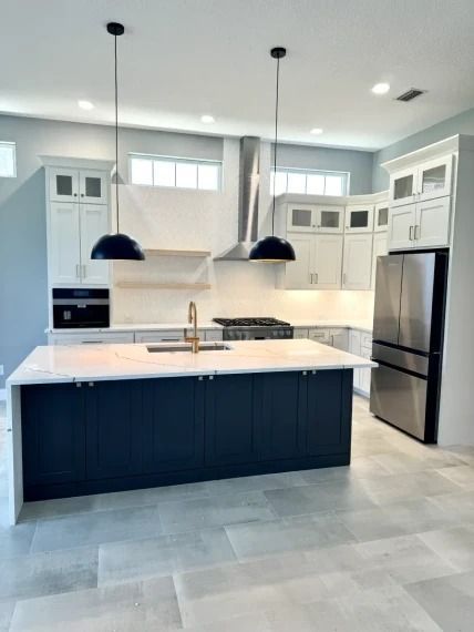 Modern white kitchen with dark island, pendant lights, stainless refrigerator, and large tiled floor