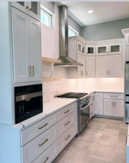 Modern white kitchen with stainless steel appliances, tall cabinets, and light countertops