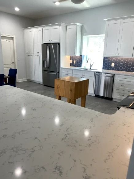 Modern kitchen with white cabinets, stainless fridge and dishwasher, and a marble island countertop