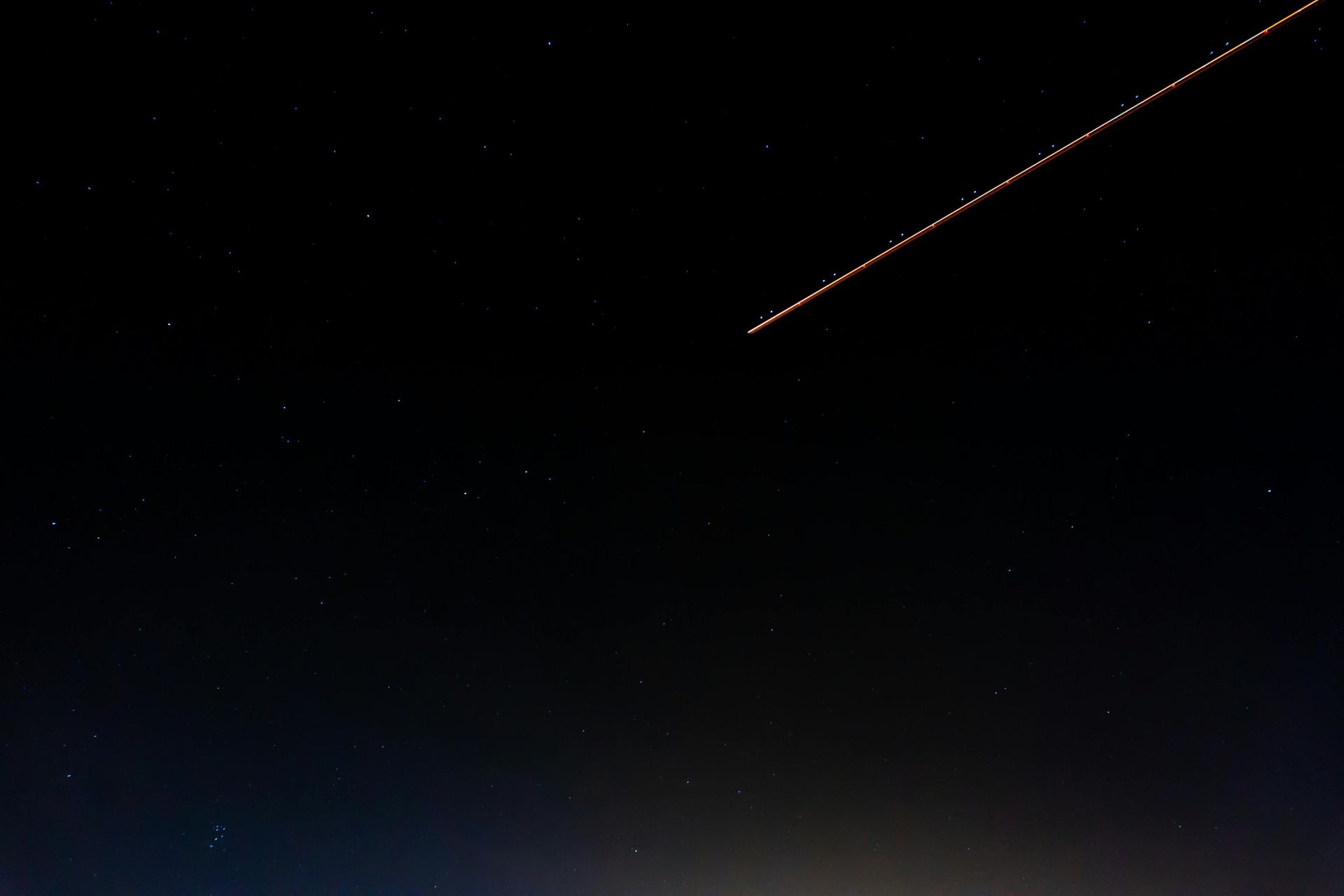 Dark night sky with a streaking trail of light; possibly a satellite or meteor shower.