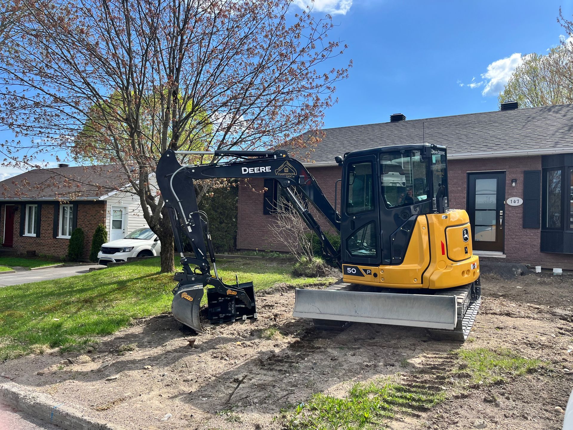 Une pelleteuse jaune est garée sur un terrain vague près d'une maison aux murs de briques brunes.