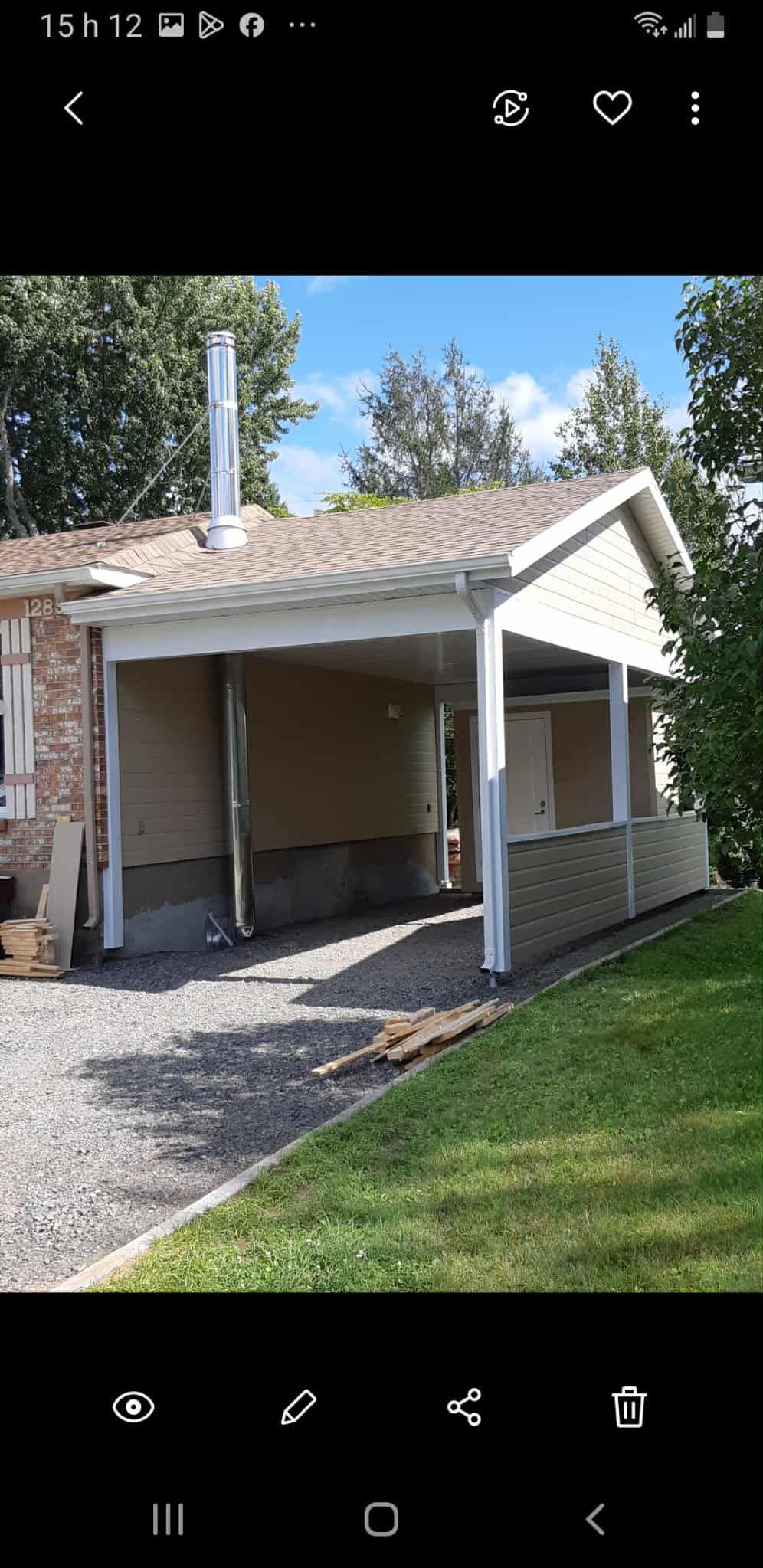 Un abri voiture avec une allée en gravier et une pelouse verte dans la cour.