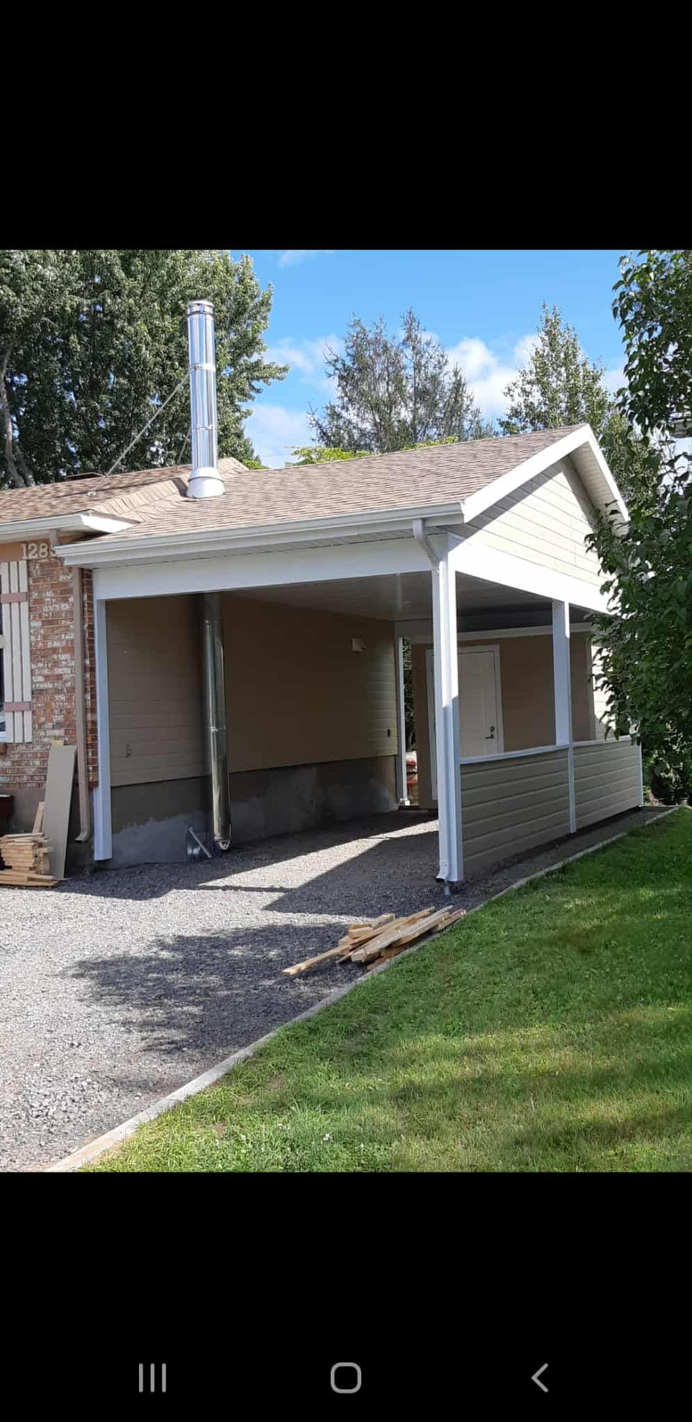 Un abri de voiture avec une allée de gravier et une pelouse verte devant une maison par une journée ensoleillée.