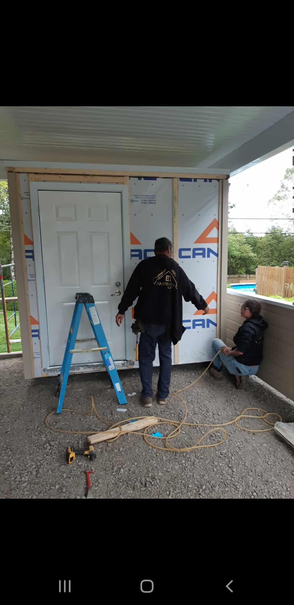 Deux personnes installent une porte. La porte est blanche, les murs sont recouverts d'isolant. L'une est debout, l'autre est assise.