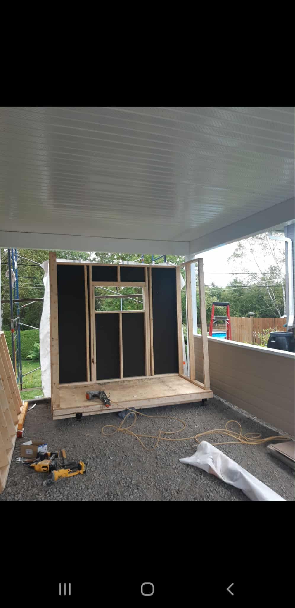 Construction d'une structure en bois avec une ouverture pour une fenêtre, sur un sol en gravier, sous un plafond blanc.