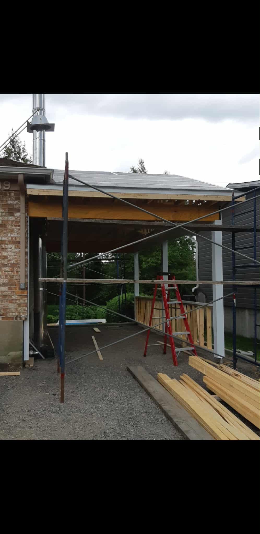 Chantier : structure partiellement construite avec une ossature en bois, un mur en briques et un sol en gravier.