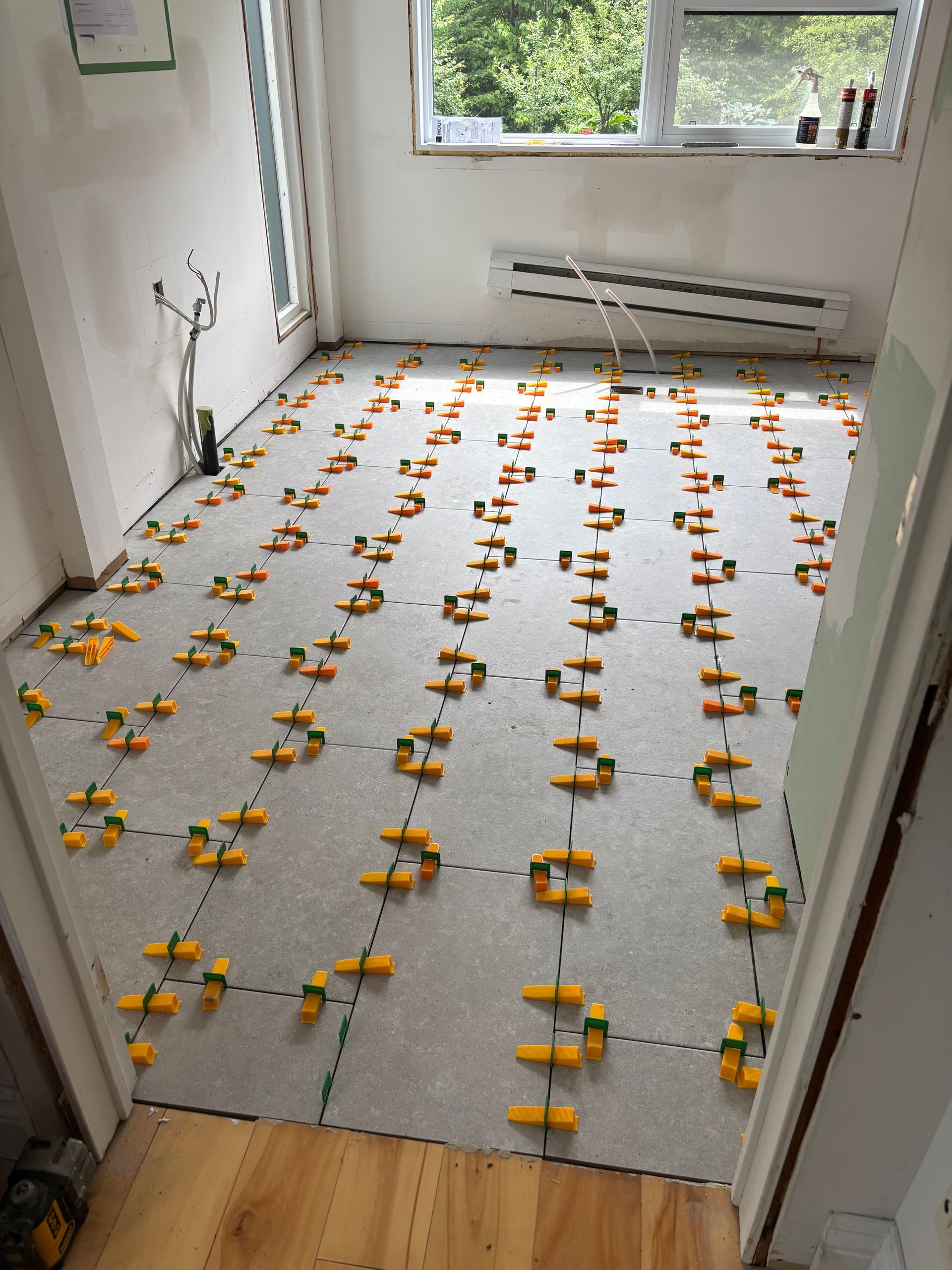 Pièce avec sol gris et clips de nivellement jaunes, prête pour la pose de carrelage.