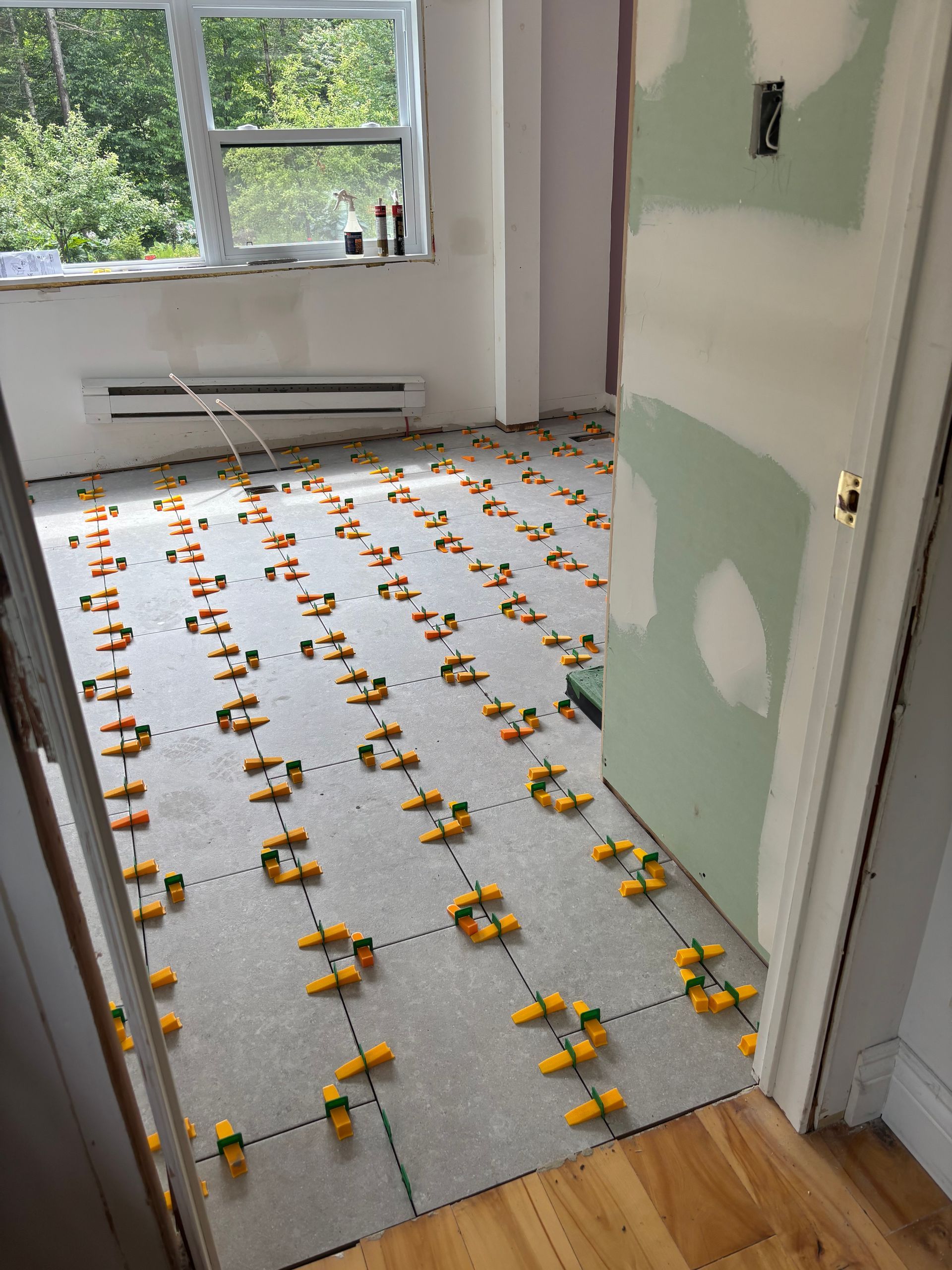 Pièce en rénovation ; carrelage posé avec système de nivellement, porte ouverte, fenêtre.