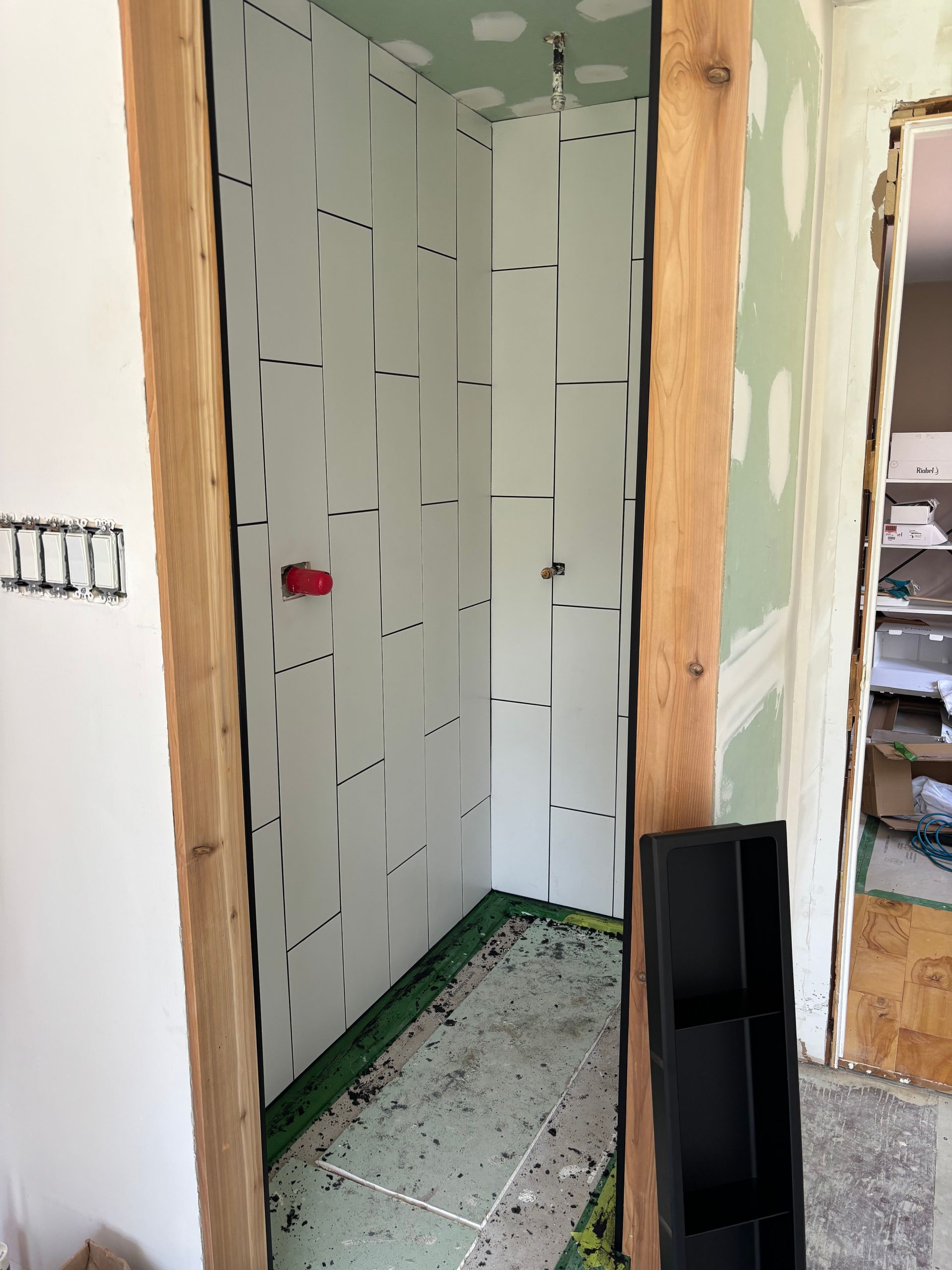 Salle de bains en construction, murs recouverts de panneaux isolants blancs, porte à cadre en bois, sol vert.