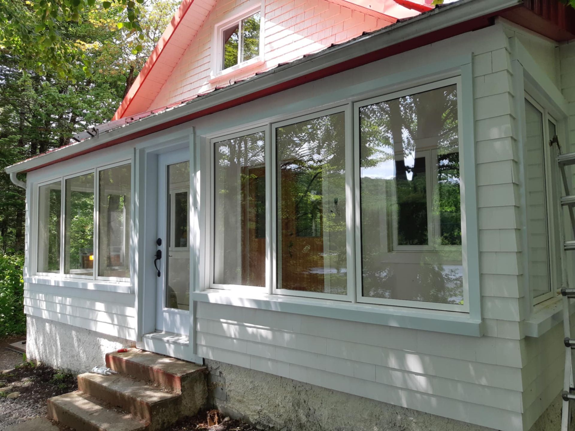 Maison blanche au toit rouge et aux fenêtres vitrées. Porche avec marches en béton.