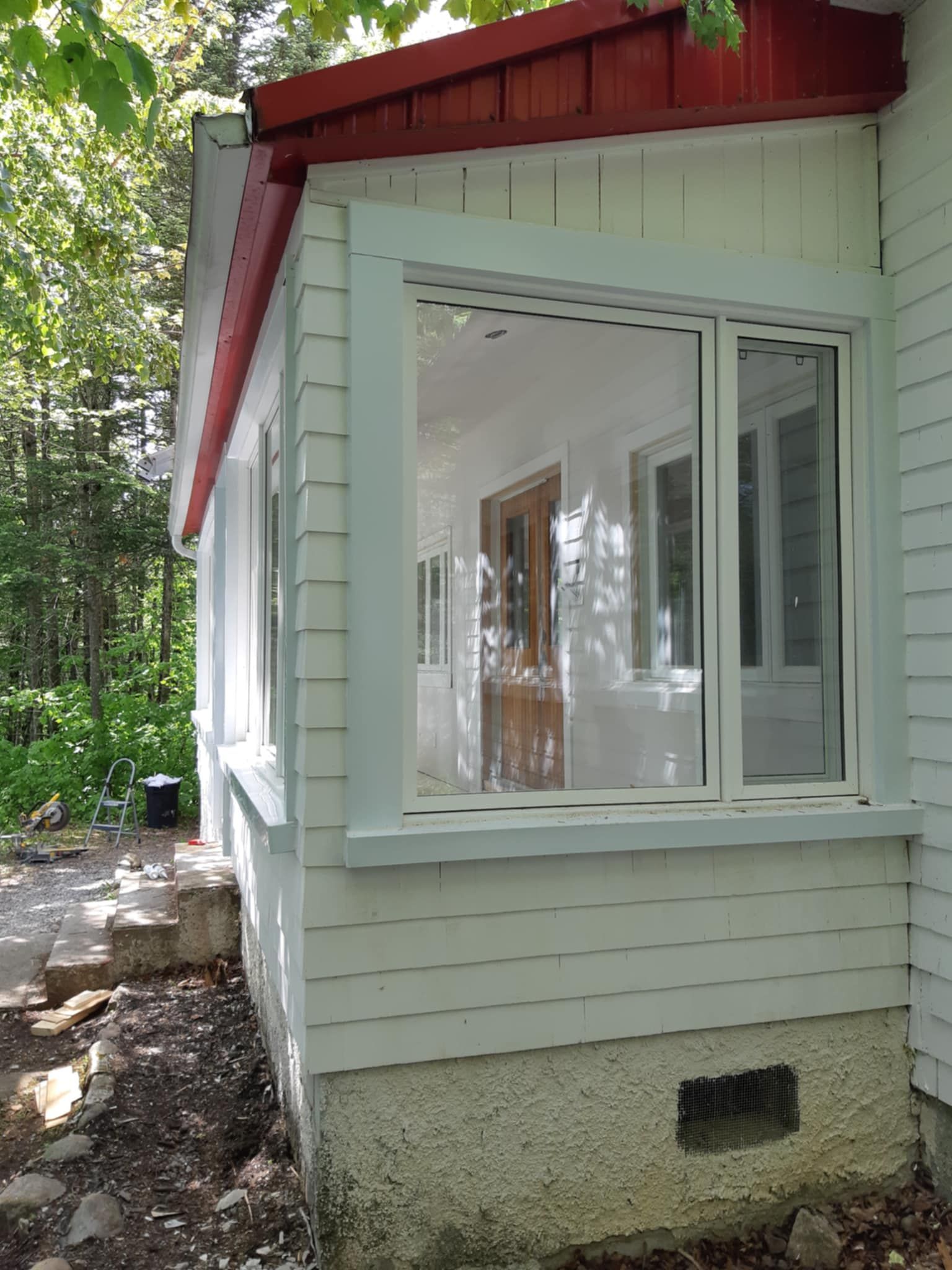 Maison blanche avec véranda grillagée, toit rouge et fondations basses en pierre, à l'extérieur.