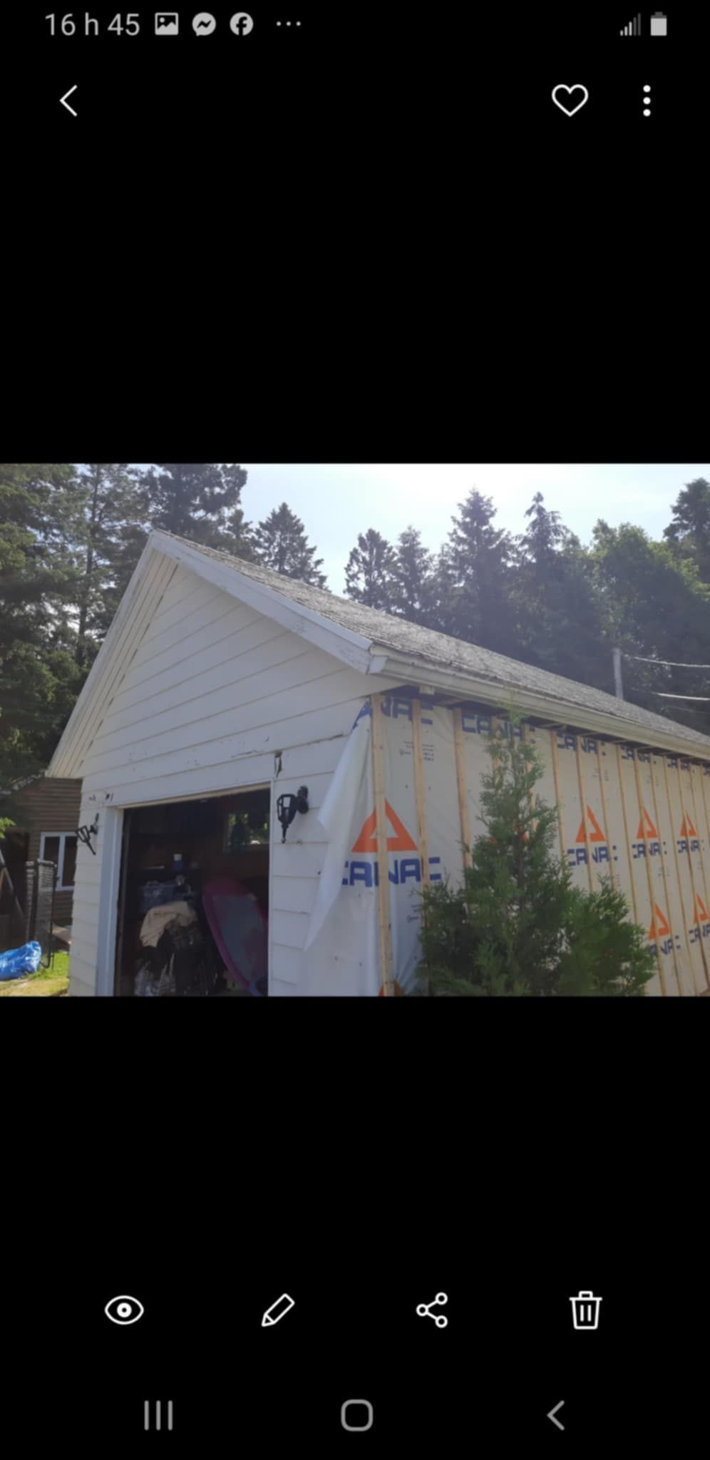 Garage blanc avec toit gris et bardage partiel, situé au milieu des arbres.
