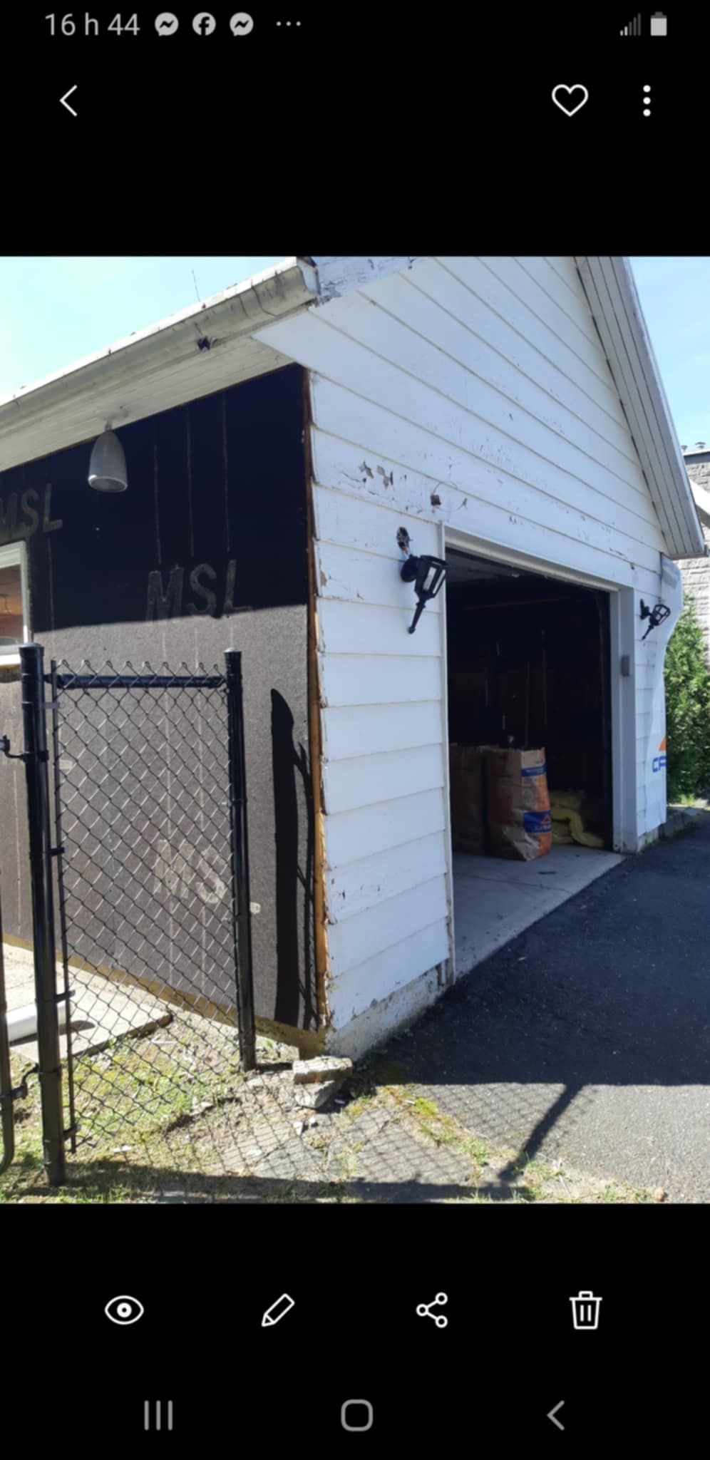 Garage blanc et noir avec porte ouverte, clôture noire devant. À l'intérieur, des sacs sont visibles.