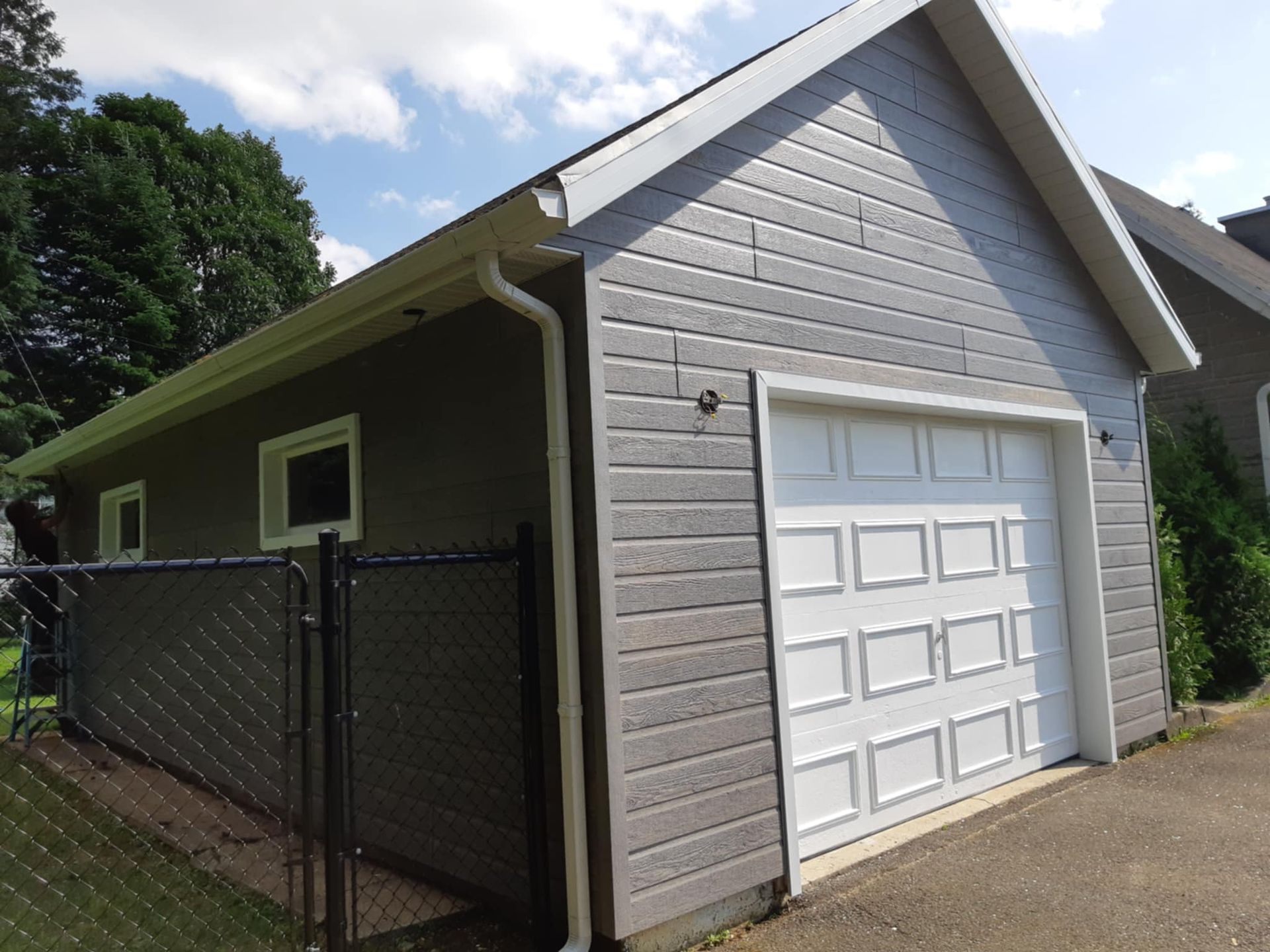 Garage gris avec porte et encadrements blancs, à côté d'une clôture noire.