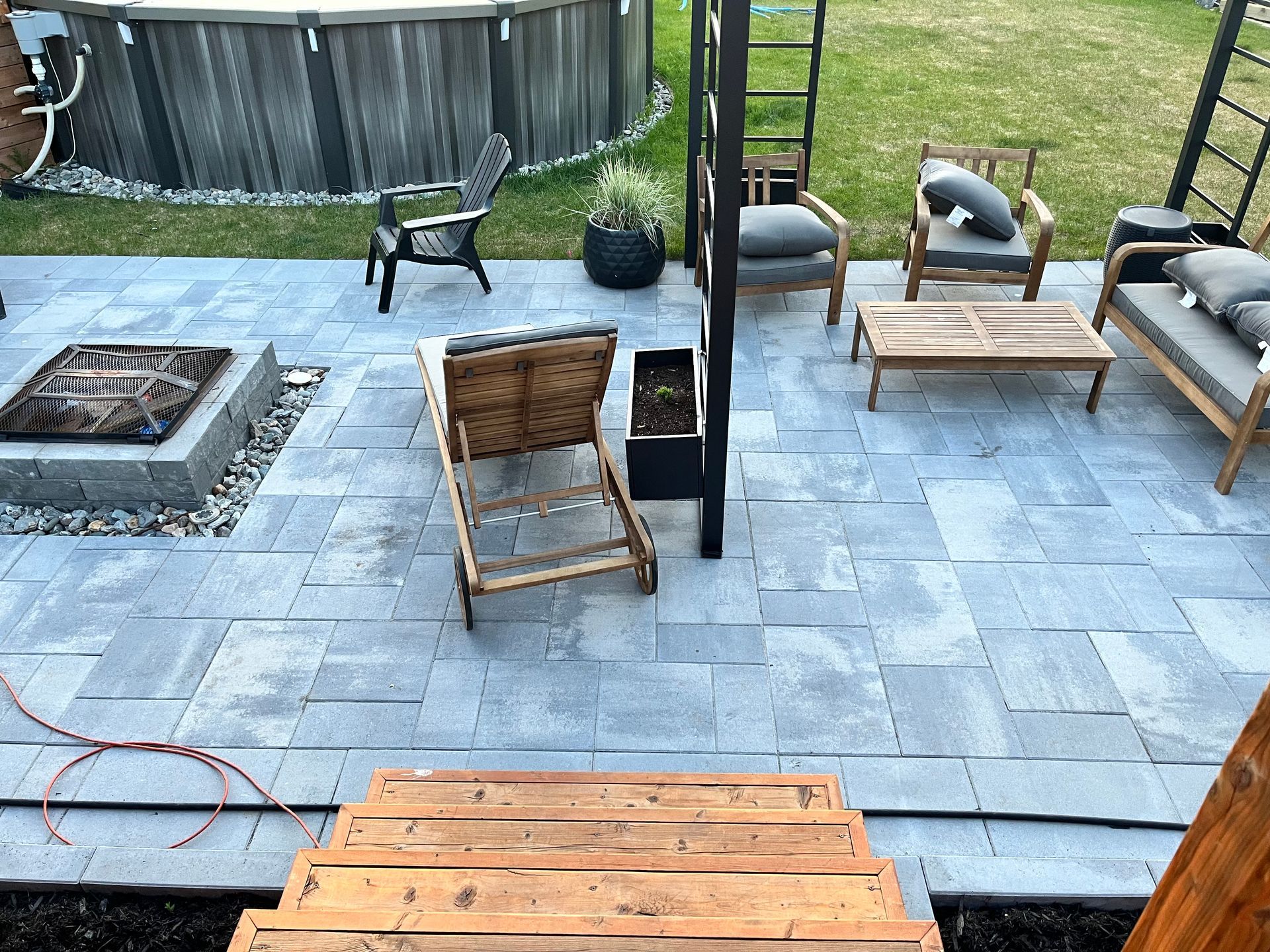 Terrasse avec dalles grises, mobilier de jardin, piscine hors sol et marches en bois.