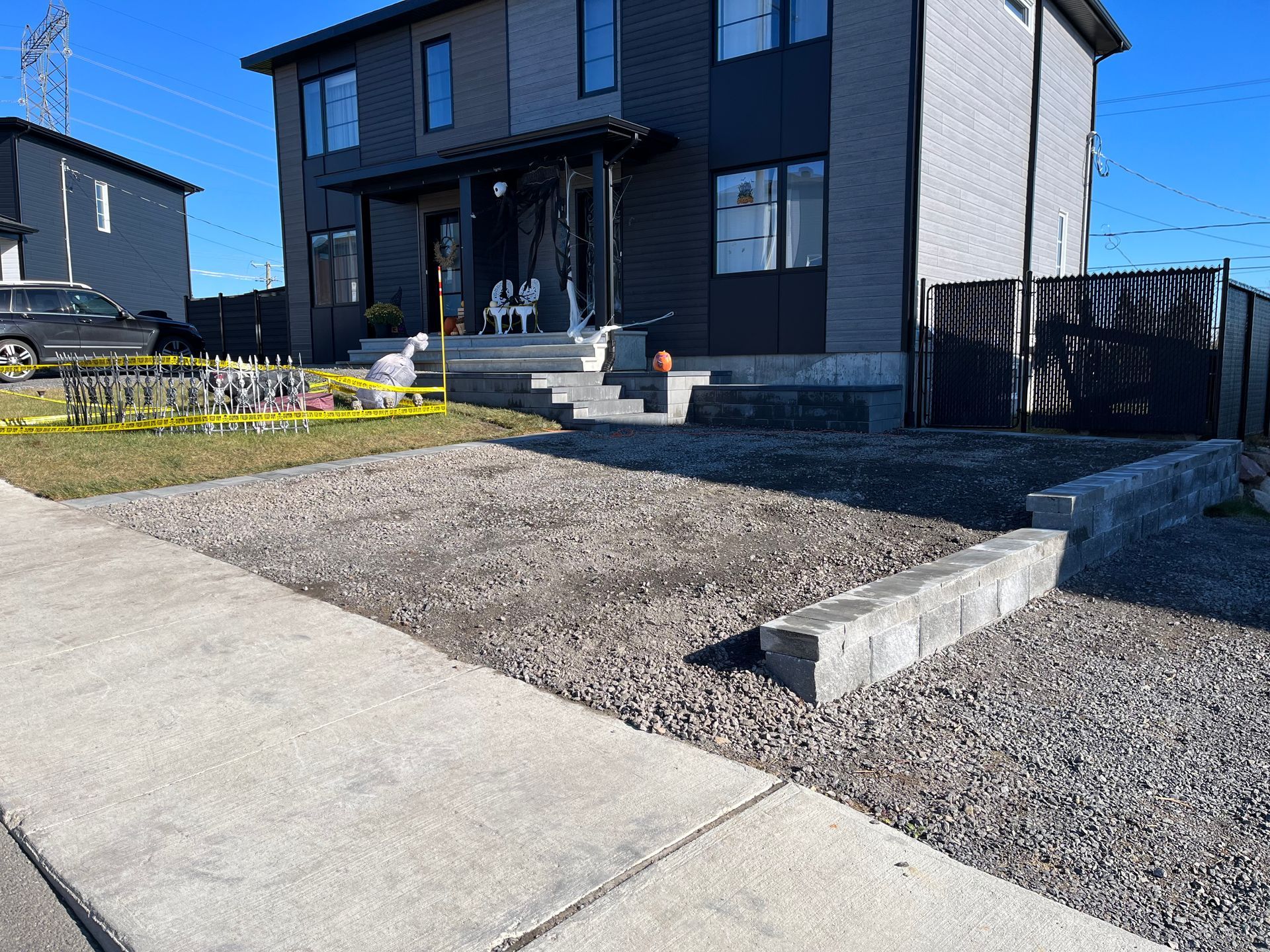 Allée en gravier devant une maison moderne. Murs de soutènement en parpaings et trottoir présents.