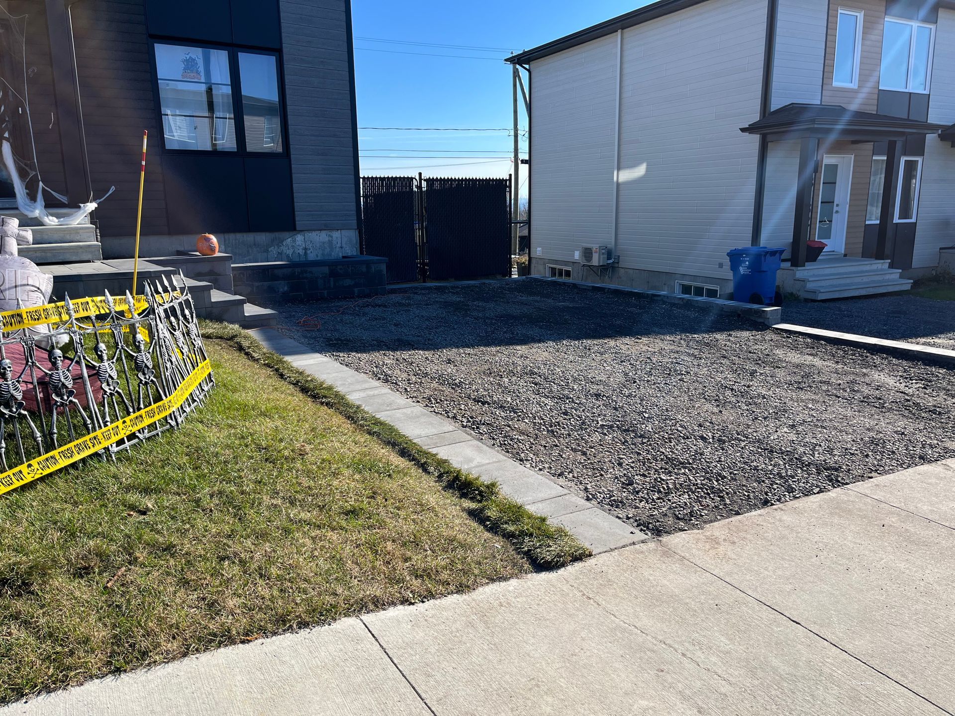 Allée de gravier bordée de béton, jouxtant une pelouse et un trottoir, avec deux maisons en arrière-plan.