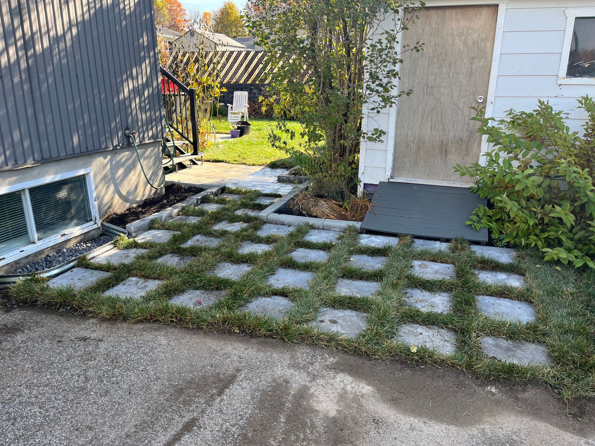 Dalles de béton avec pelouse, à côté d'un bâtiment et d'arbustes.