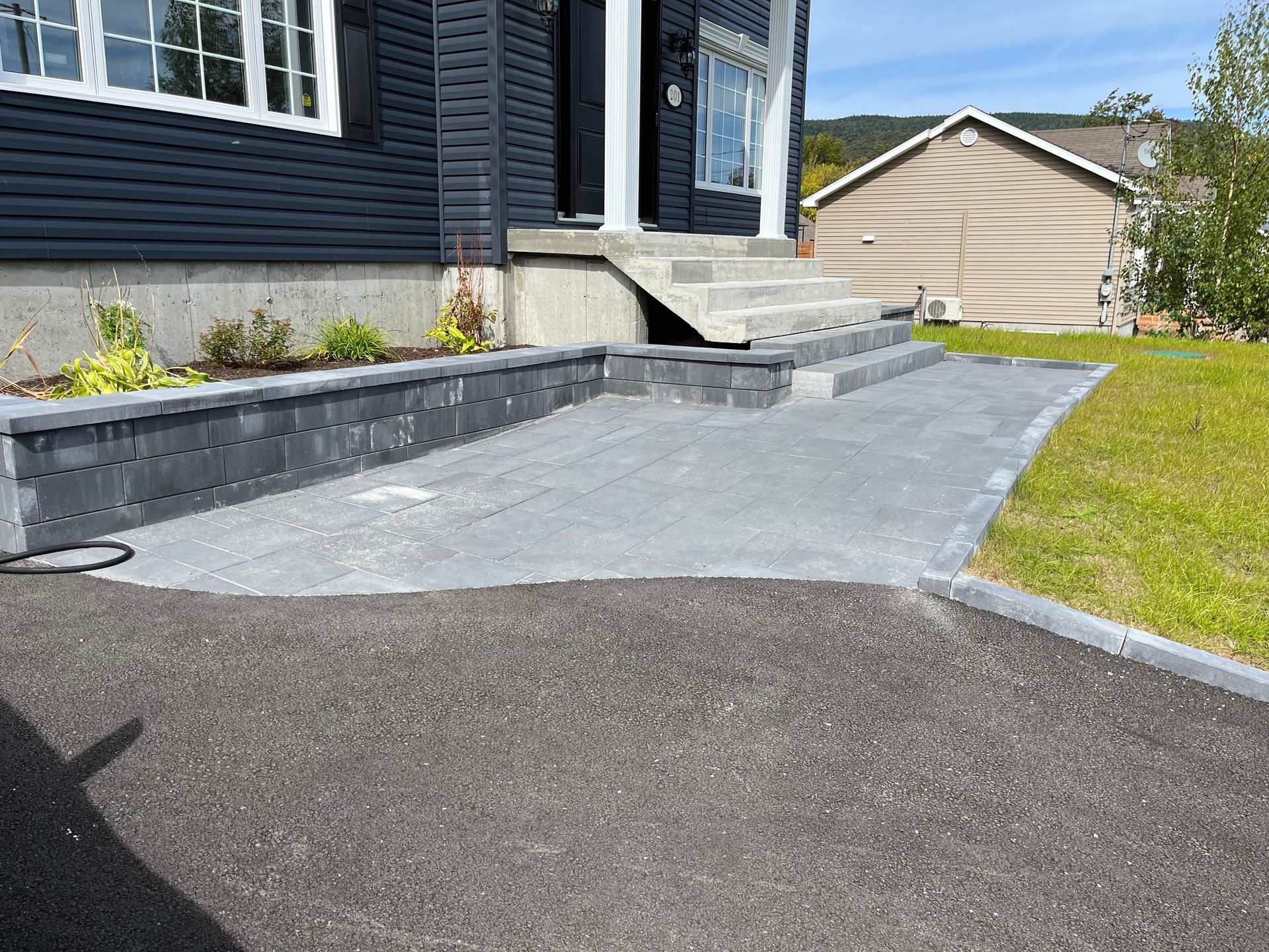 Allée asphaltée et chemin piétonnier en béton menant à une maison au revêtement foncé.