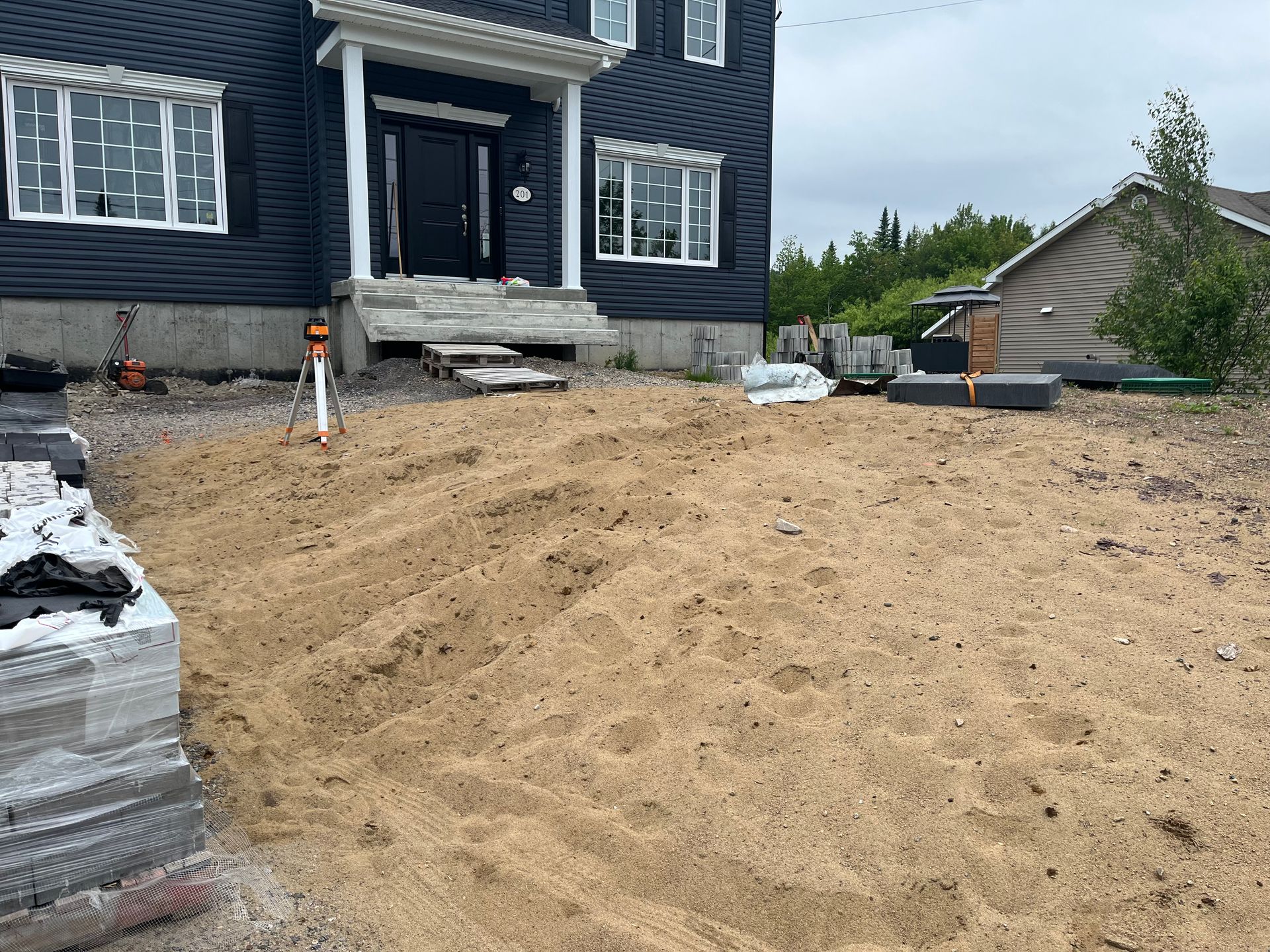 Projet d'aménagement paysager avec du sable en cours sur l'extérieur de la maison.