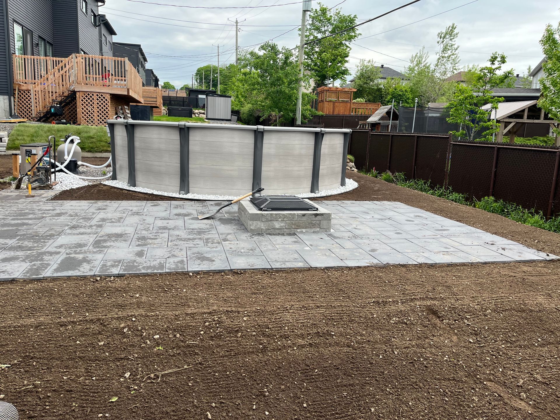 Piscine hors sol dans le jardin. Dalles grises autour d'un foyer extérieur en béton. Pelouse fraîchement semée.