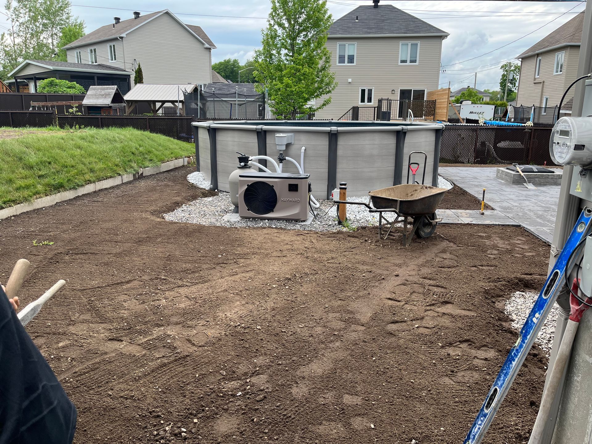 Cour arrière avec une piscine hors sol partiellement construite, de la terre, des matériaux d'aménagement paysager et des maisons environnantes.