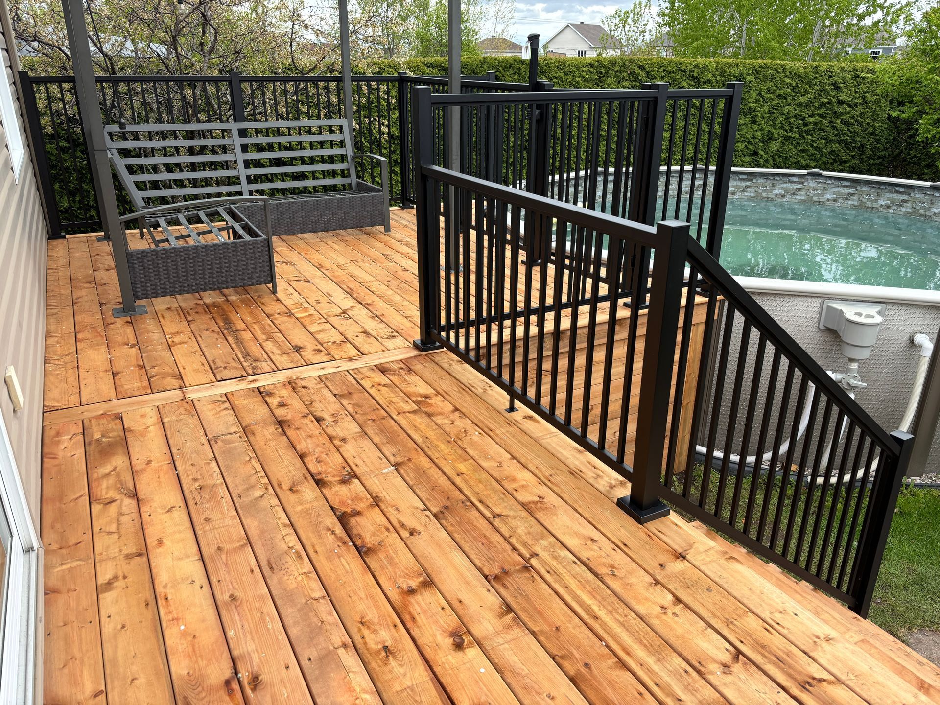 Terrasse en bois avec rambarde noire, donnant sur une piscine.