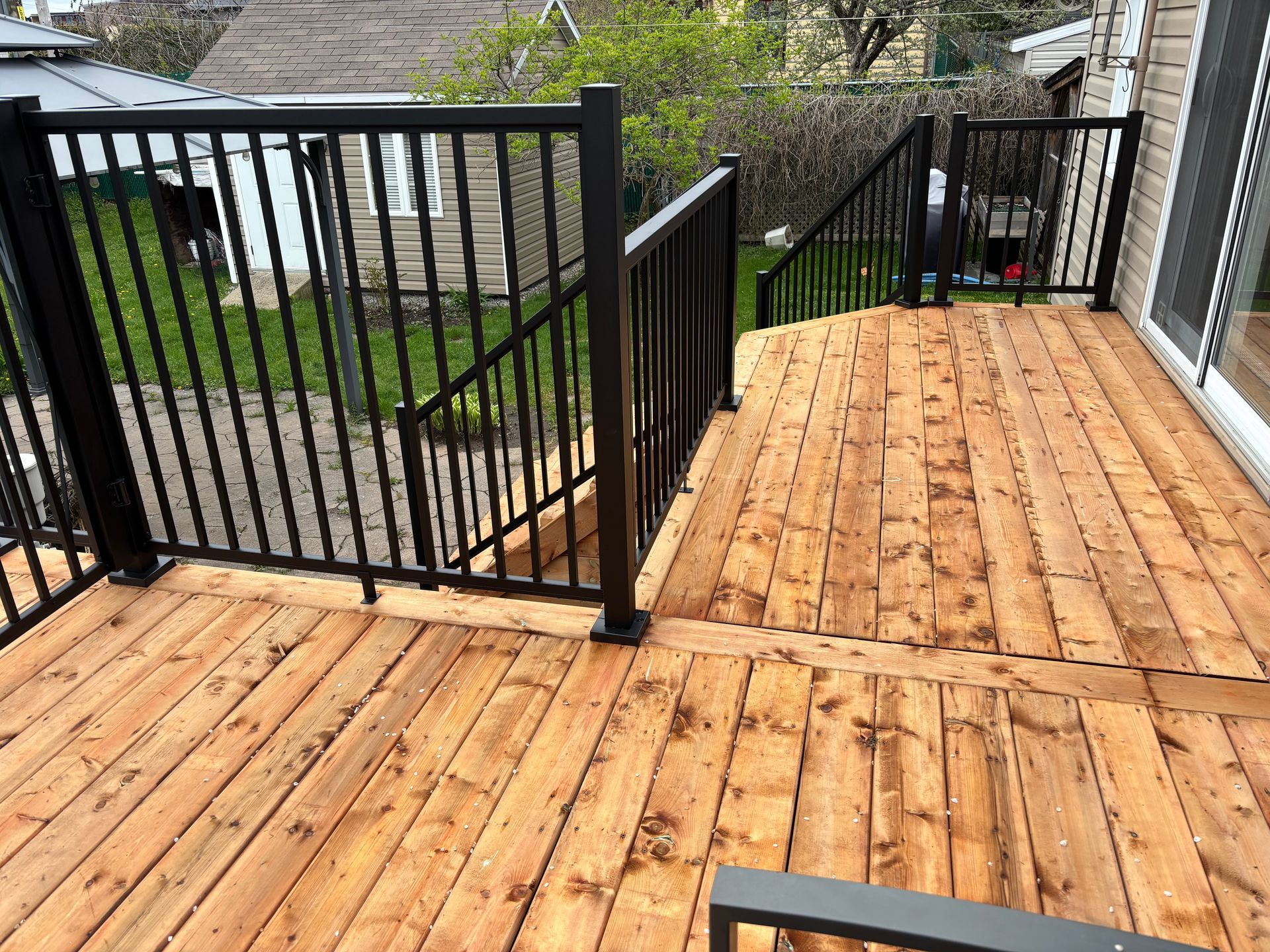 Terrasse en bois avec rambarde noire et marches menant à une cour.