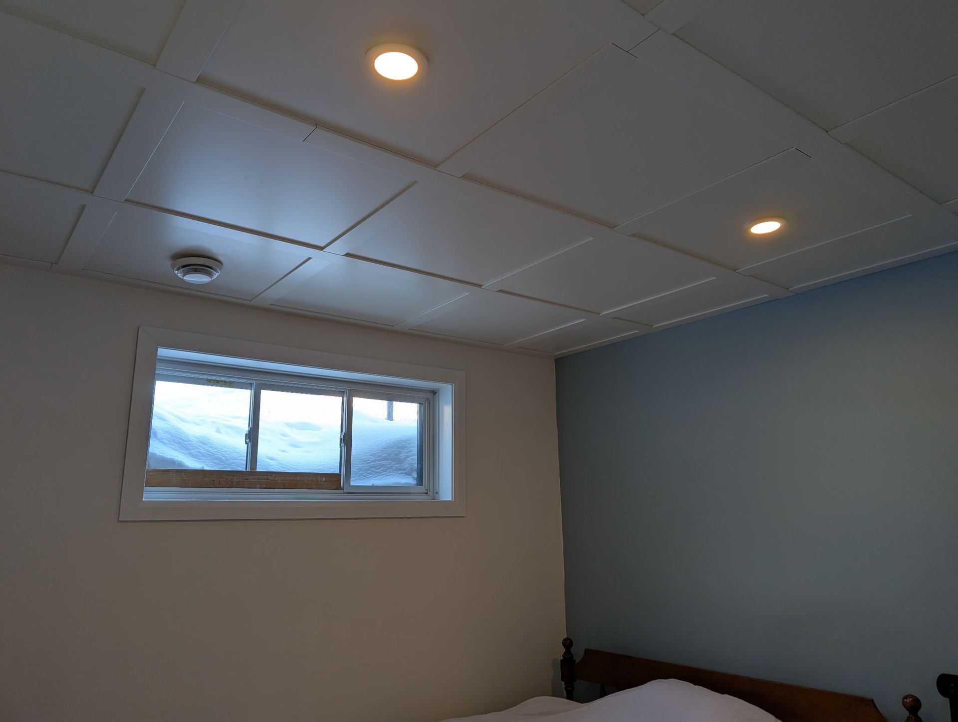 Intérieur de la chambre : plafond blanc avec spots encastrés, petite fenêtre, murs bleus et blancs.