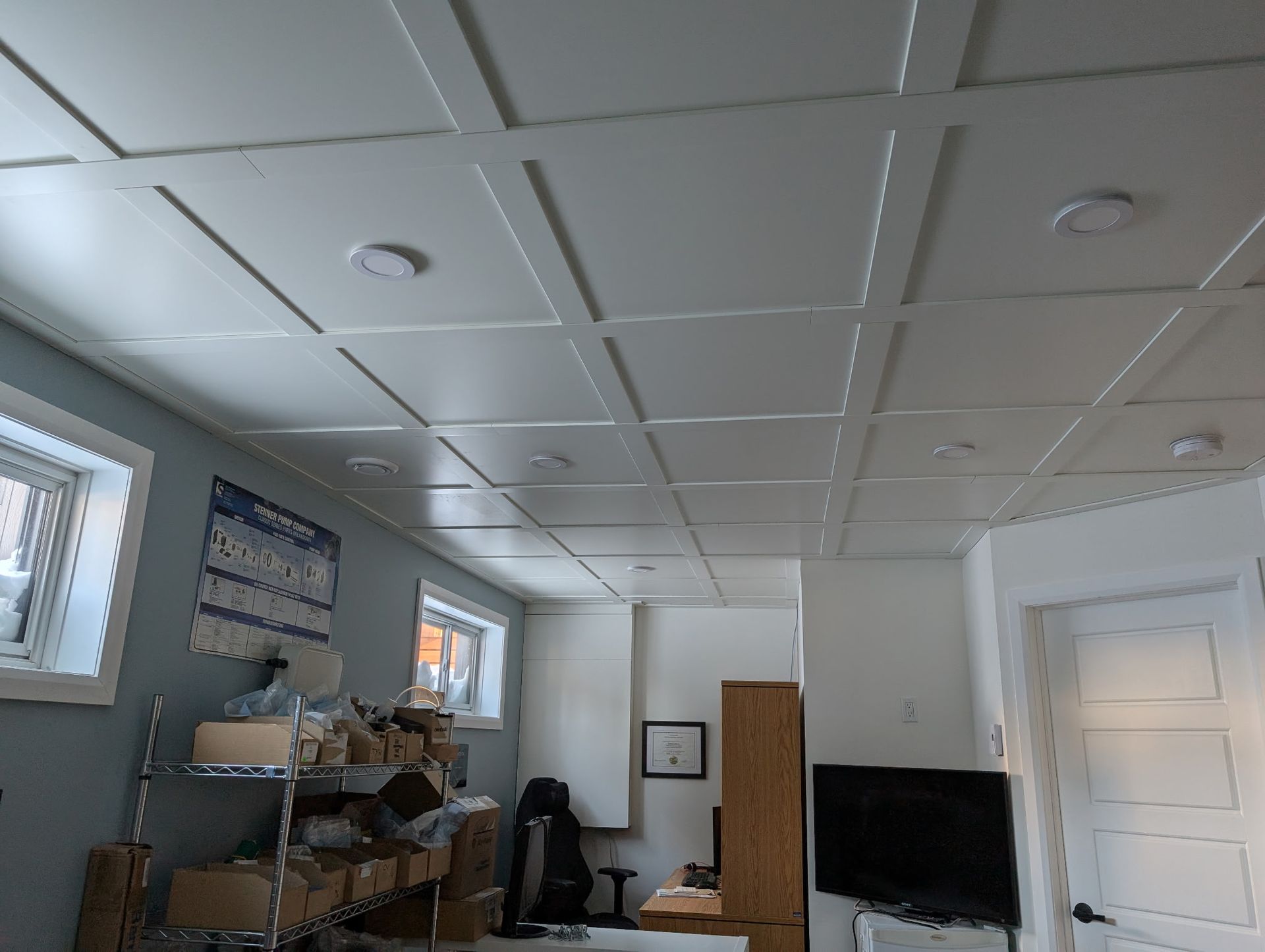 Plafond à panneaux blancs avec spots encastrés, dans une pièce baignée de lumière.