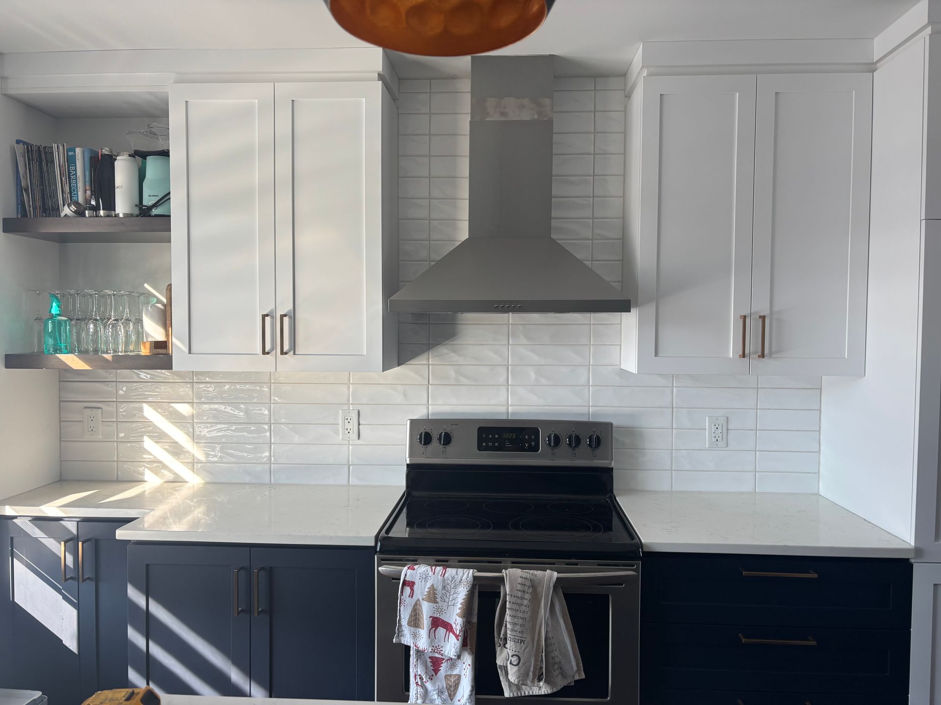 Cuisine avec armoires blanches, armoires basses bleu marine, électroménagers en acier inoxydable et crédence en carrelage blanc.