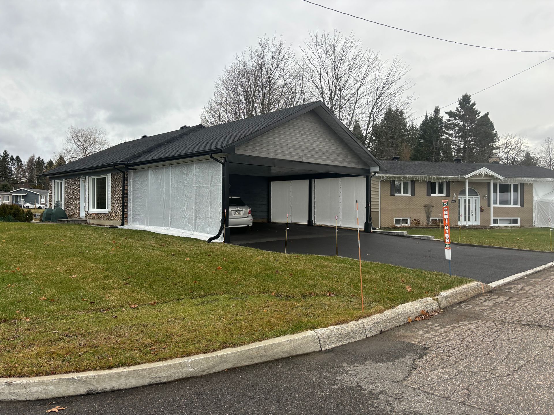 Maison avec abri voiture ; une voiture est garée à l'intérieur. Pelouse et ciel couvert.
