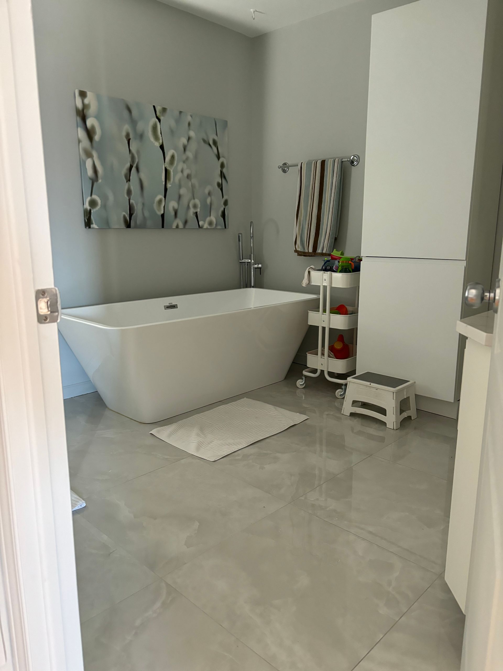 Salle de bains moderne avec baignoire blanche, carrelage gris clair et décoration murale.