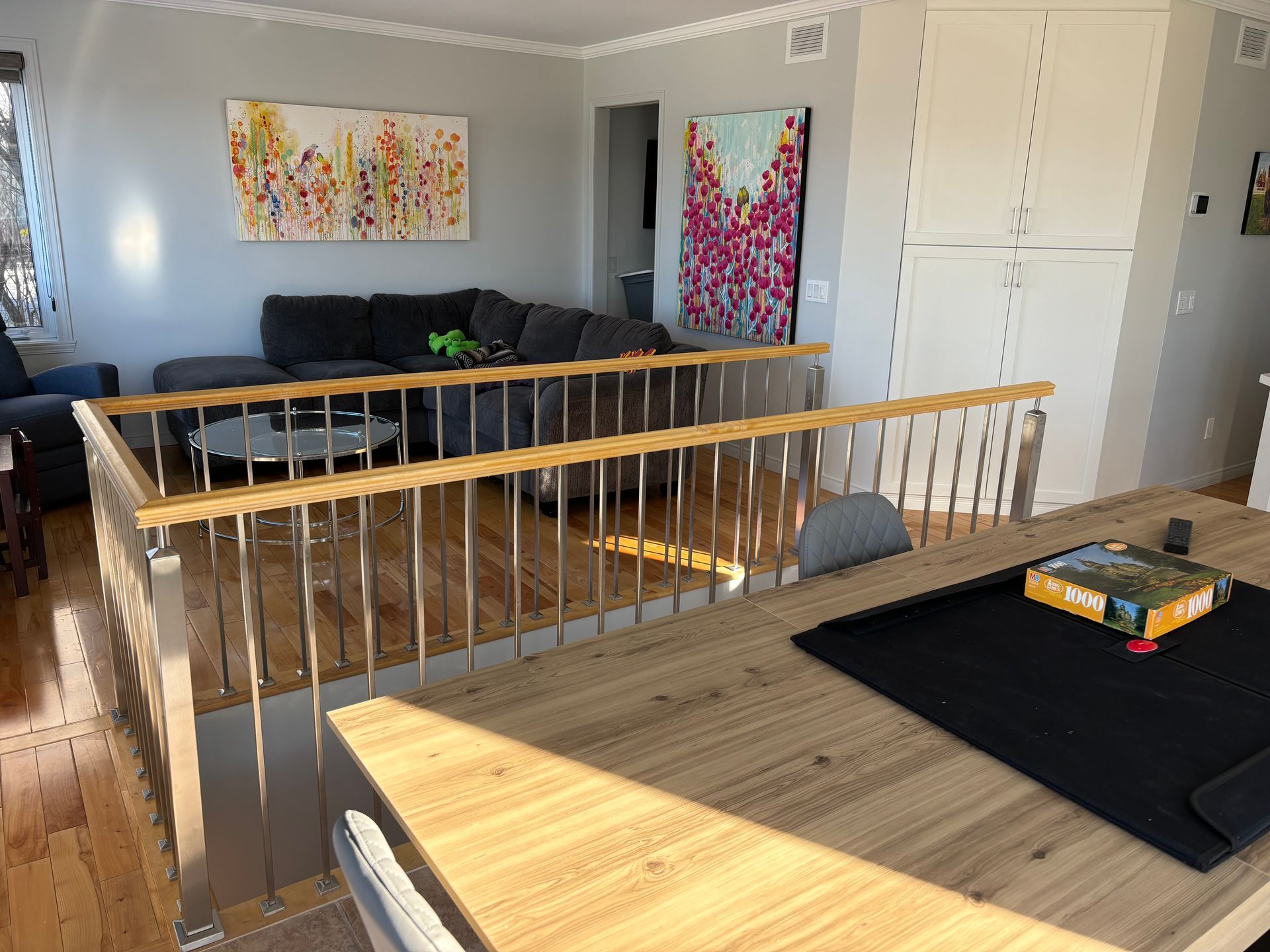 Salon avec vue partielle sur la cuisine. Un plancher surélevé est muni d'une rambarde. Des œuvres d'art ornent les murs.