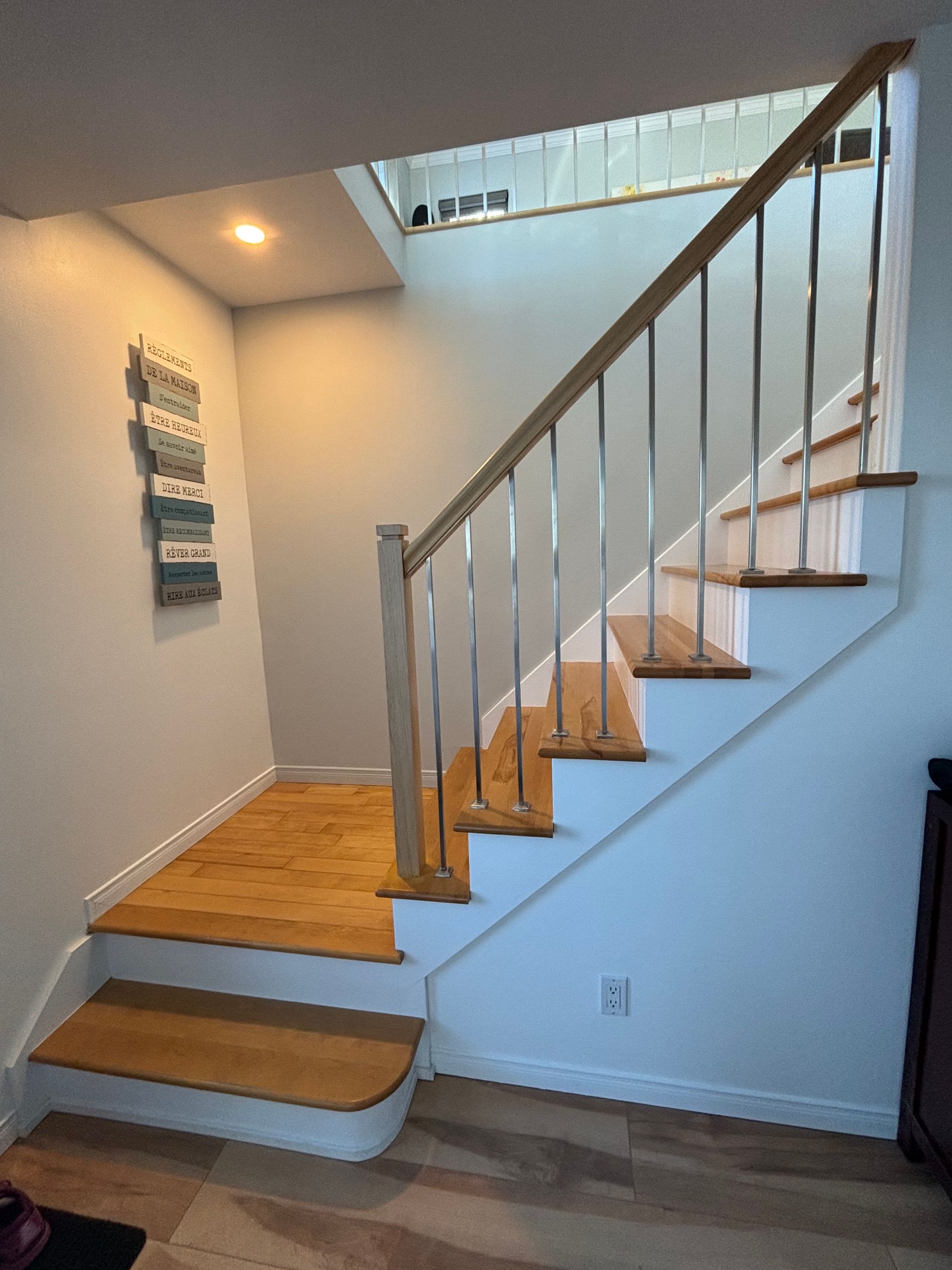 Escalier avec marches et rampe en bois, balustres en acier inoxydable. Murs clairs, éclairage zénithal et œuvres d'art sur le thème de l'océan.