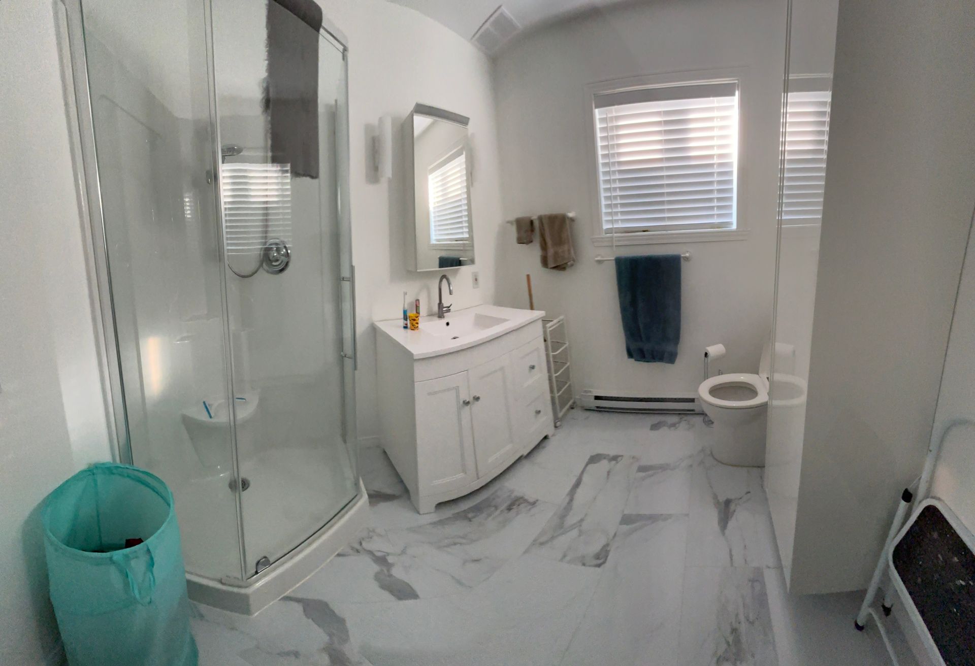 Salle de bains moderne avec sol et murs en marbre blanc et gris. Comprend une douche en verre, un meuble-lavabo, des toilettes et une fenêtre.