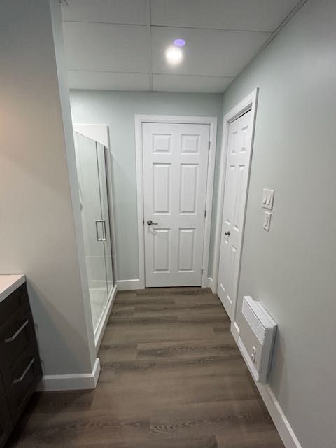 Couloir étroit aux murs bleu clair, sol gris imitation bois, portes blanches et douche en verre.