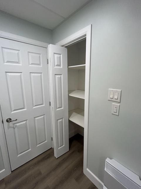 Un placard de rangement avec des étagères blanches et une porte blanche entrouverte, à côté d'une autre porte blanche sur un mur gris.