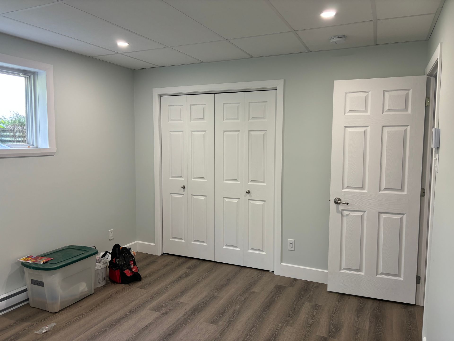 Pièce vide avec portes blanches, placard et murs peints ; une fenêtre fermée se trouve à gauche.