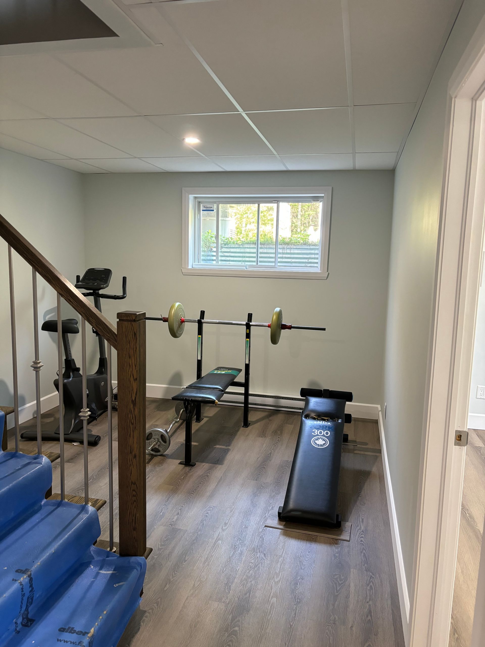Salle de sport à domicile avec banc de musculation, barre d'haltères, vélo d'appartement et revêtement de sol imitation bois.