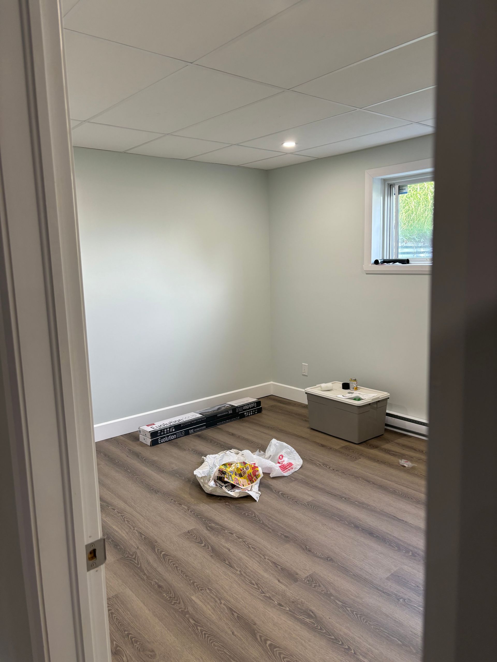 Pièce vide aux murs vert pâle, avec un nouveau revêtement de sol imitation bois et une petite fenêtre.