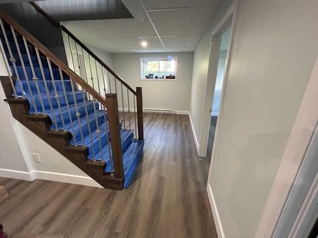 Vue intérieure : Escalier avec marches recouvertes de bleu, rampe en bois et murs gris, menant à un couloir avec un sol imitation bois.