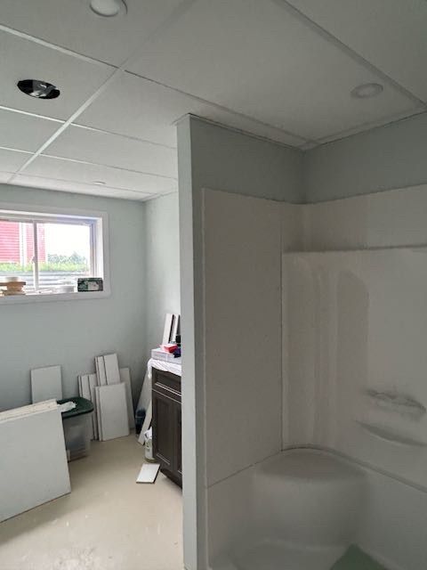 Rénovation de salle de bain. Murs bleu clair, douche et plafond blancs. Espace non aménagé avec fenêtre et équipements.