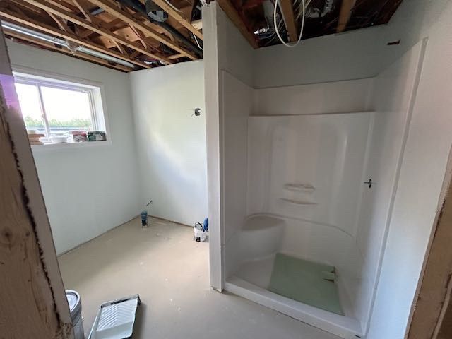 Salle de bains en construction avec cabine de douche, petite fenêtre et plafond non fini.