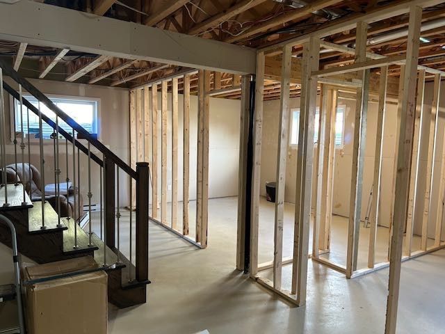 Ossature du sous-sol avec escalier sur la gauche. Intérieur non fini avec charpente apparente.