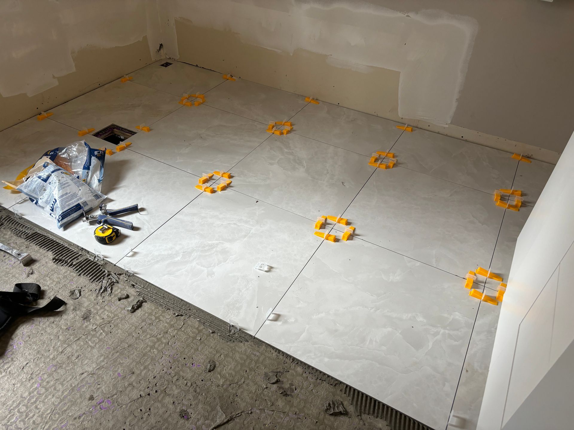 Pose de grands carreaux gris au sol de la salle de bains, à l'aide de clips de nivellement.