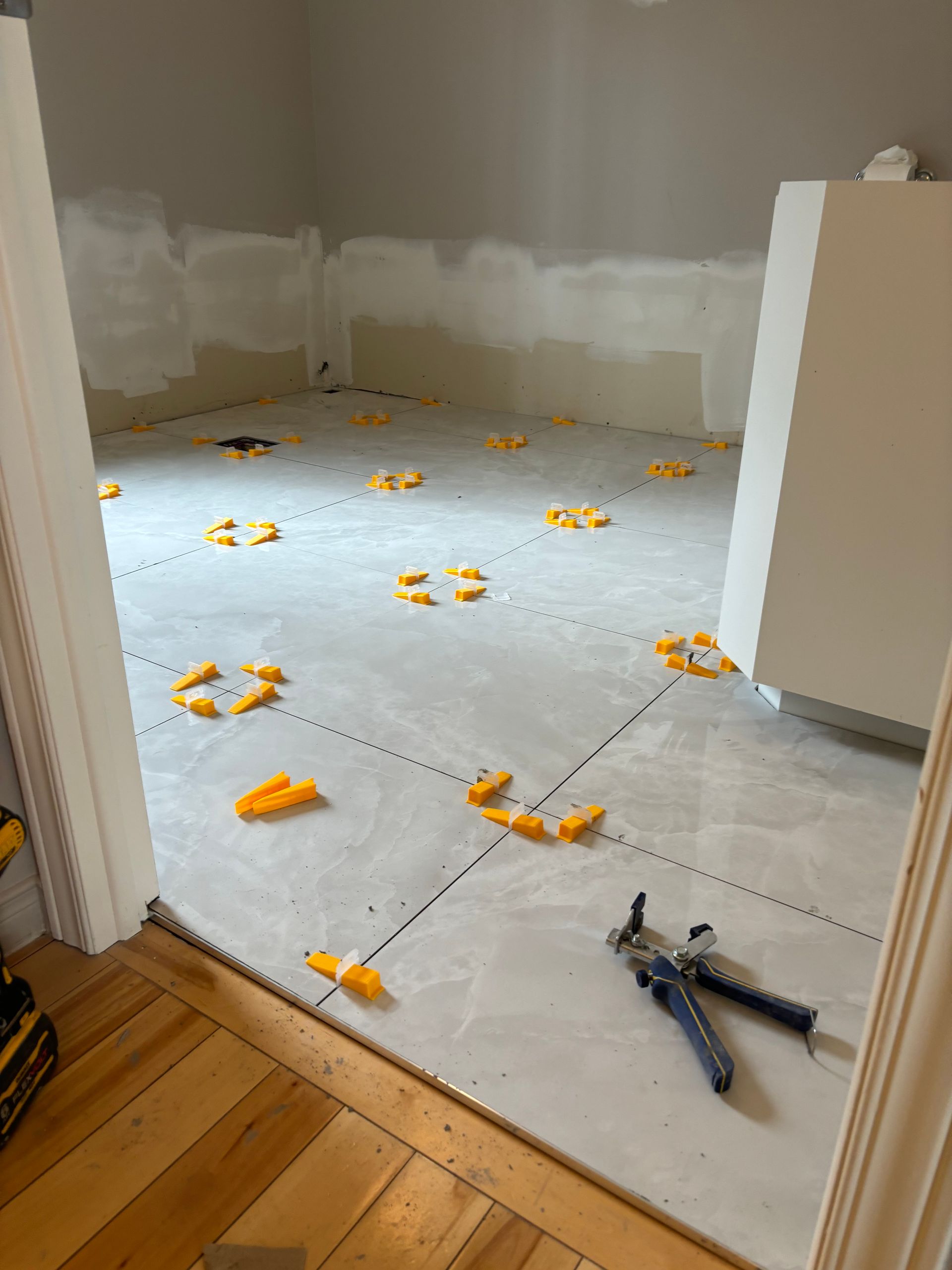 Pièce en construction avec carrelage gris au sol, clips de nivellement et outils.
