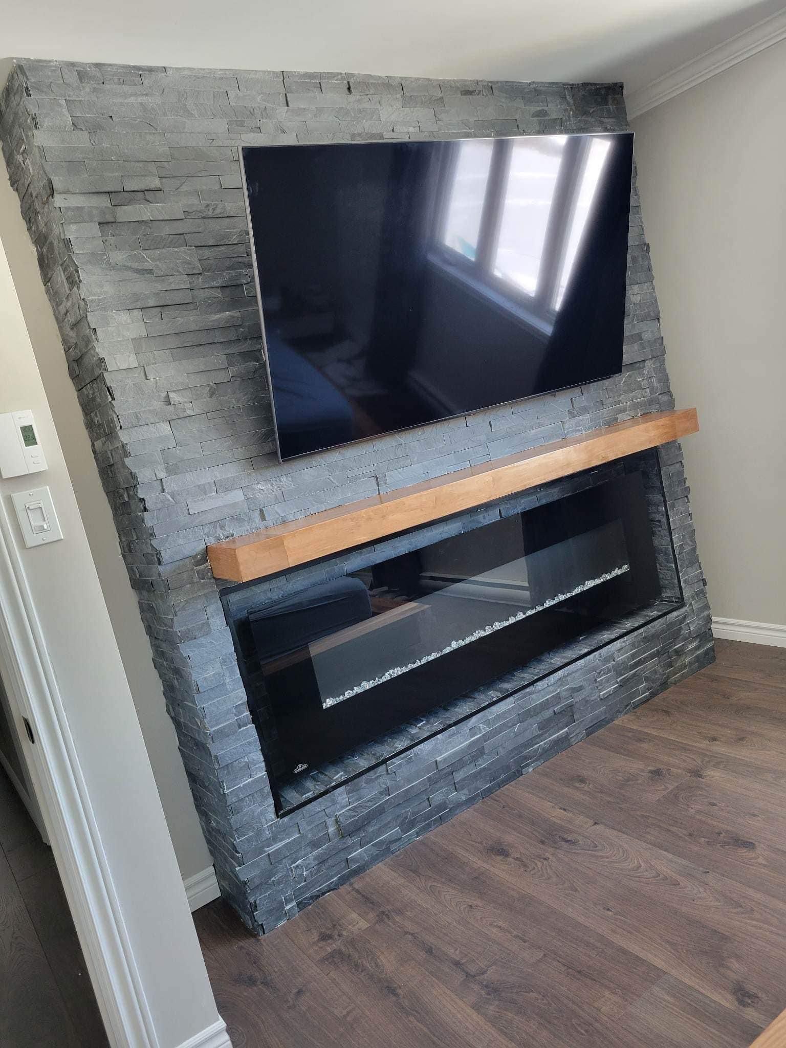 Cheminée moderne avec entourage en pierre grise, télévision noire et manteau de cheminée en bois.